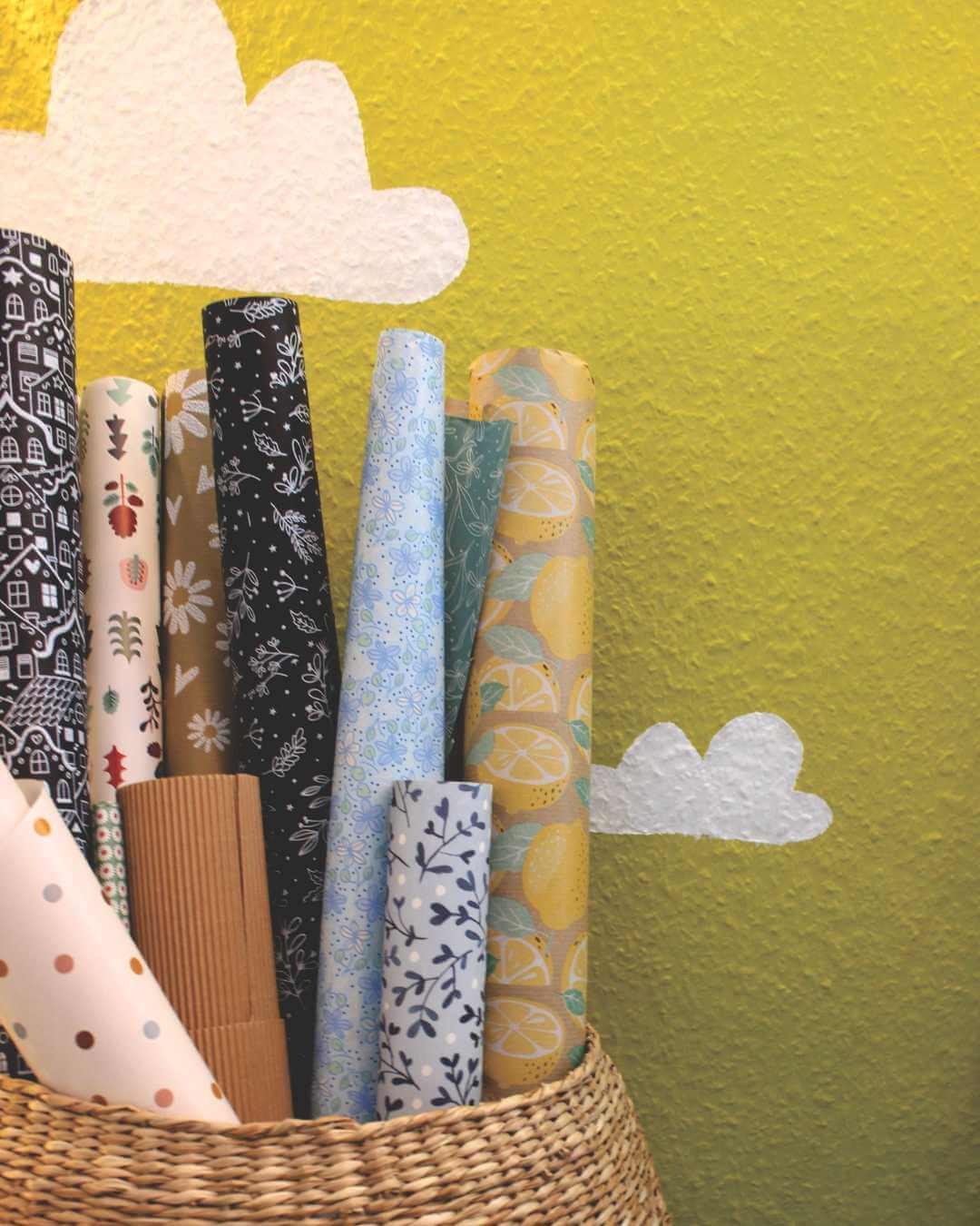 korb-mit-geschenkpapier-vor-gelber-wand-mit-weissen-wolken-Atelier-Sintje-Tramm